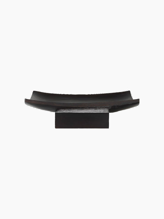 A front view of the Releve Platter. A long, rectangular dish in black wood with curved ends, resting on a solid block base.