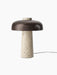 An angled view of the Reverse Table Lamp, showing its textured travertine stone base and smooth, bronzed aluminium shade.
