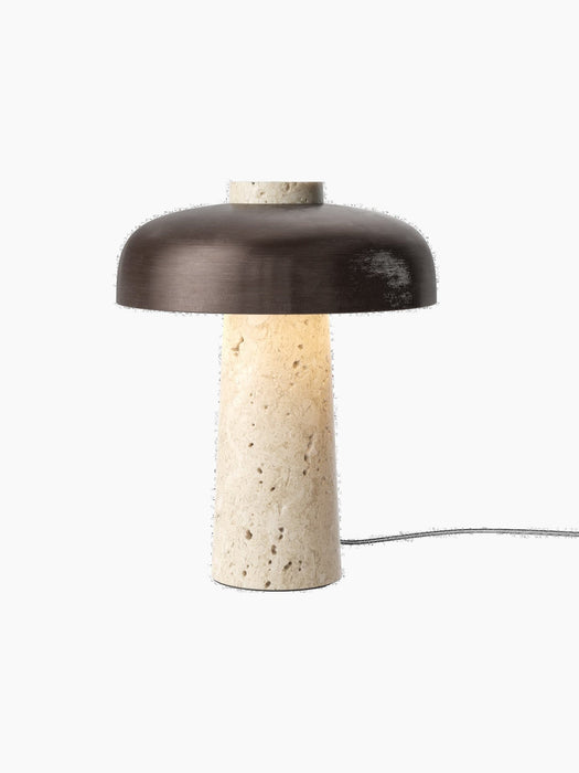 The Reverse Table Lamp seen from an angle. It has a porous, light travertine stone base and a dark bronzed aluminium shade.