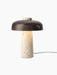 The Reverse Table Lamp seen from an angle. It has a porous, light travertine stone base and a dark bronzed aluminium shade.