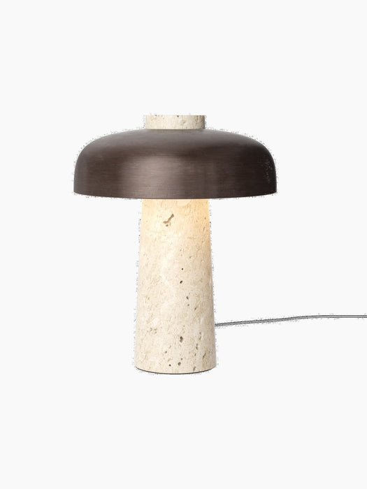 Front view of the Reverse Table Lamp with its lit, conical travertine base and a wide, curved bronzed aluminium shade.