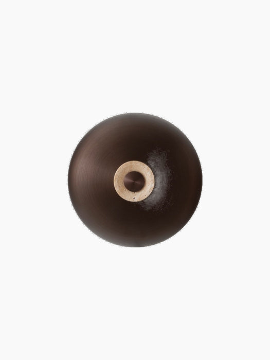 The Reverse Wall Lamp, front-on against a black background, with a bronzed aluminium shade and travertine base.