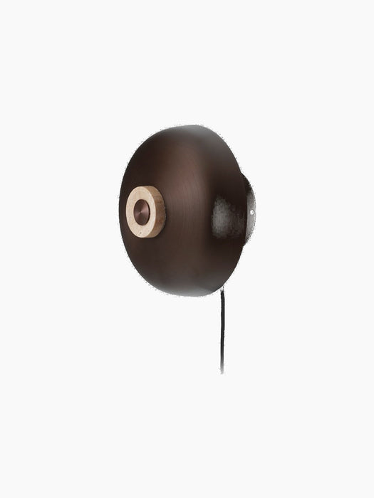 An angled shot of the Reverse Wall Lamp on a black background, showing its bronzed aluminium shade and travertine dimmer.