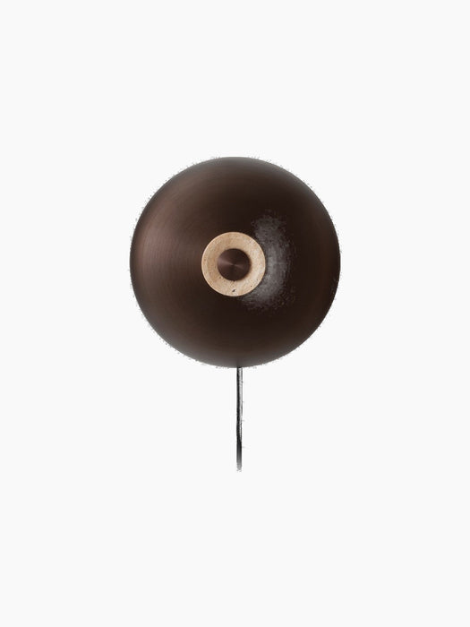 A front view of the Reverse Wall Lamp, with a circular bronzed aluminium shade and a central travertine base with a dimmer.