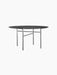A round, black Snaregade Dining Table with a black oak veneer top and minimalist black steel base, on a black background.