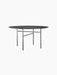 A black, round Snaregade Dining Table with a thin top and a slender, geometric steel base, shown against a black background.