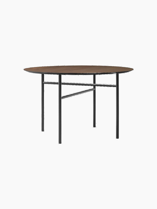 An angled view of the Snaregade Dining Table, Round, featuring a dark stained oak top and a geometric black steel base.