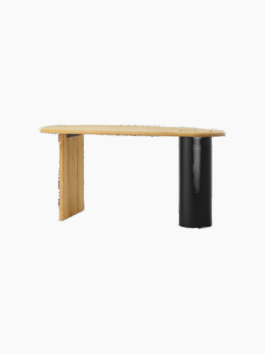 The Eclipse Desk in natural oiled oak, seen at an angle, highlighting its asymmetrical top, flat leg, and black column leg.