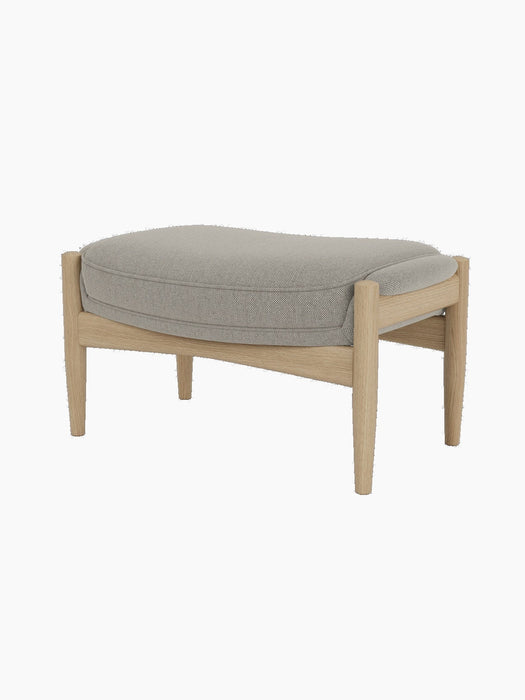 A side view of The Seal Ottoman, featuring a light grey upholstered cushion on a mid-century modern frame of natural oak.
