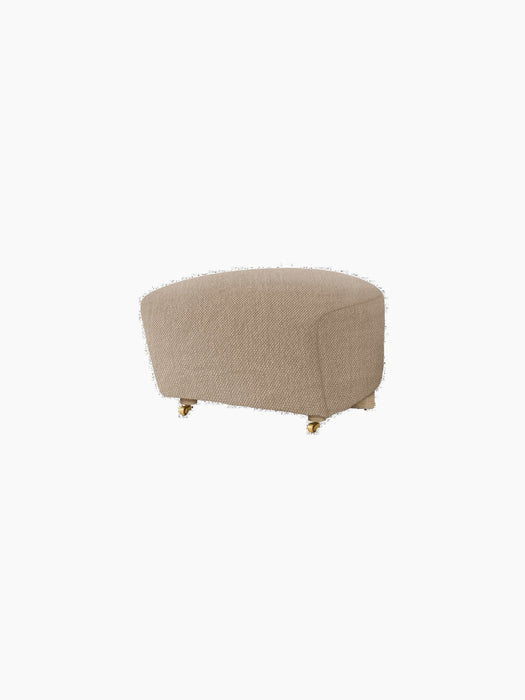 The Tired Man Ottoman in a beige textile with natural oak legs and brass casters, shown from an angle on a black background.