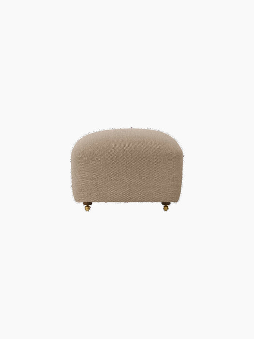 Front view of The Tired Man Ottoman in a light brown textile with a rounded shape, wooden legs, and front brass casters.