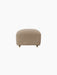 Front view of The Tired Man Ottoman in a light brown textile with a rounded shape, wooden legs, and front brass casters.