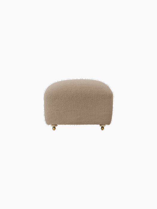 Front view of The Tired Man Ottoman, upholstered in a beige textile. Rounded ottoman has natural oak legs with brass casters.