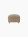 Front view of The Tired Man Ottoman, upholstered in a beige textile. Rounded ottoman has natural oak legs with brass casters.