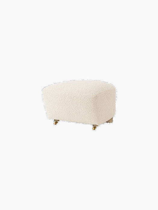 An angled view of The Tired Man Ottoman, upholstered in an off-white, textured Logan Flint fabric on a black background.