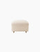A front view of The Tired Man Ottoman, upholstered in a plush, off-white textile, with light oak legs and brass casters.