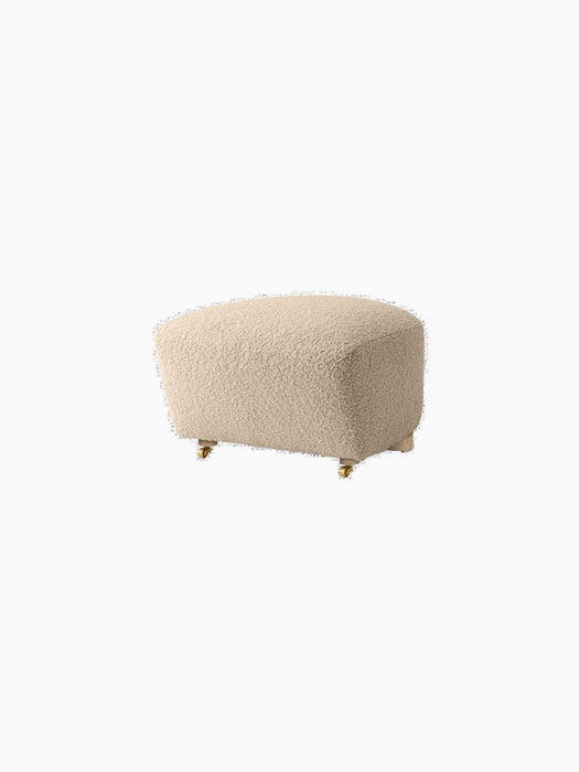The Tired Man Ottoman in a light, plush textile, with light wooden back legs and brass casters on the front.