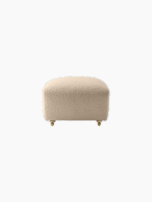 Front view of The Tired Man Ottoman upholstered in a light, textured textile, with natural oak legs and front brass casters.