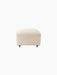 Front view of The Tired Man Ottoman upholstered in cream-coloured textured textile, with short legs and small brass casters.