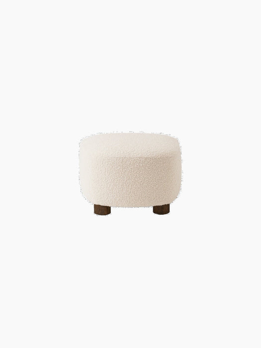 Back view of The Tired Man Ottoman in plush, off-white textile. It has a rounded shape and sits on four short, dark oak legs.