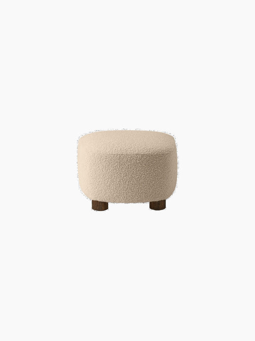 Back view of The Tired Man Ottoman, upholstered in a cream textured textile, showing its rounded shape and dark wooden legs.