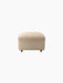 A front view of The Tired Man Ottoman, featuring its plush, off-white textured upholstery and short legs with brass casters.