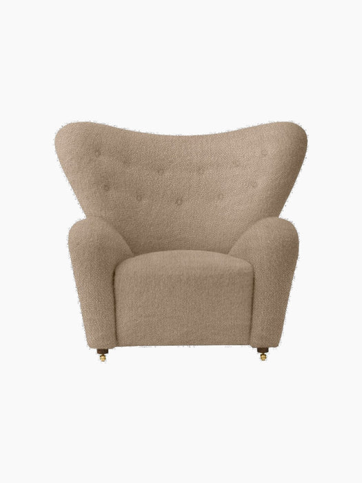 Front view of The Tired Man Lounge Chair upholstered in a textured beige textile, with a high curved back and brass castors.