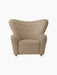 Front view of The Tired Man Lounge Chair upholstered in a textured beige textile, with a high curved back and brass castors.