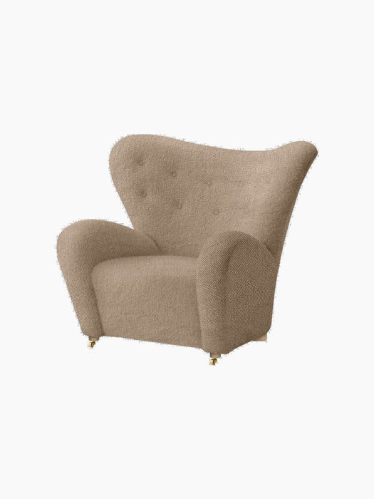 The Tired Man Lounge Chair in light brown textile, with a high, curved back and brass castors.