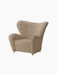 The Tired Man Lounge Chair in light brown textile, with a high, curved back and brass castors.