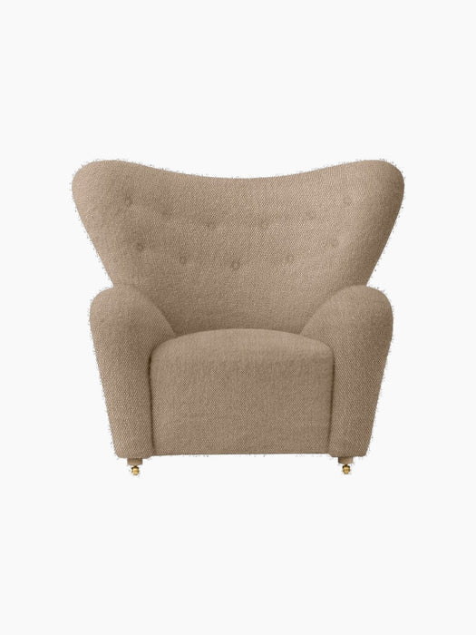Front view of The Tired Man Lounge Chair in light brown textile. It has a high, winged back, rounded arms, and brass castors.