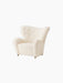 An angled view of The Tired Man Lounge Chair in a textured off-white textile, showing its curved high back and brass castors.