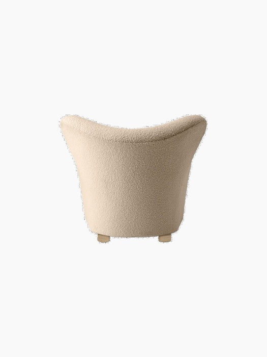 Back view of The Tired Man Lounge Chair in a light textured textile, showing its curved backrest and short wooden legs.