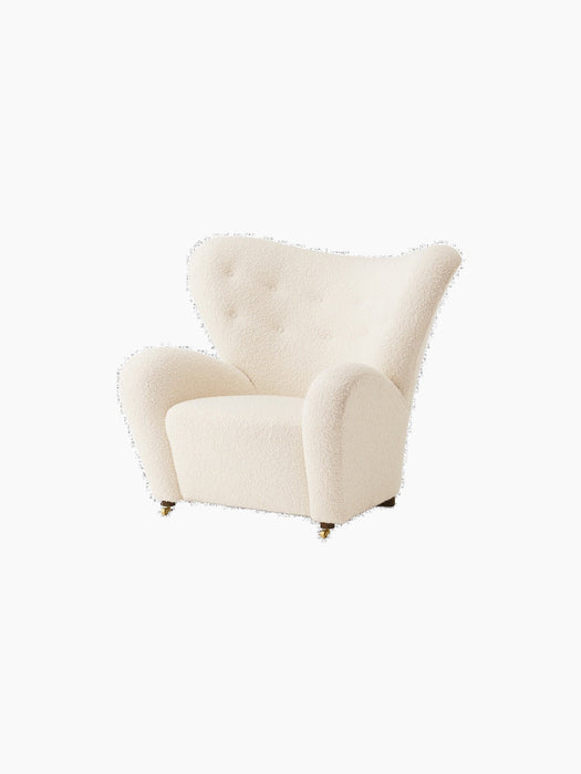 An angle view of The Tired Man Lounge Chair upholstered in a cream-coloured, textured textile against a black background.