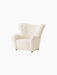 An angle view of The Tired Man Lounge Chair upholstered in a cream-coloured, textured textile against a black background.