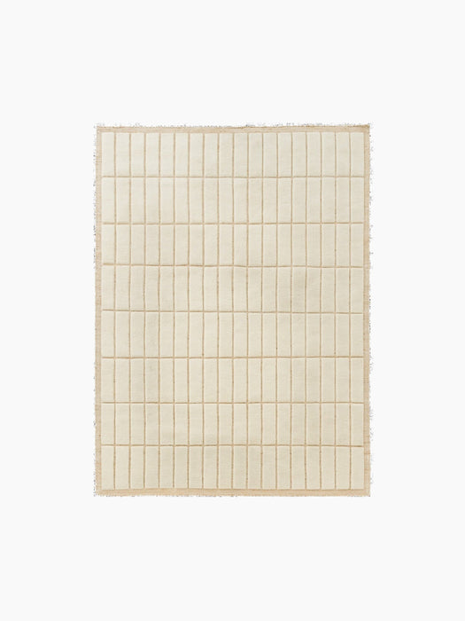 Top-down view of a square, light beige rug featuring a raised grid pattern of soft, rectangular tiles and a woven border.
