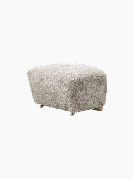 A Tired Man Ottoman footstool upholstered in light green Green Tea sheepskin, shown at an angle on a plain black background.