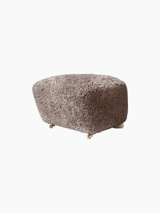 Three-quarter view of The Tired Man Ottoman in Sahara sheepskin, a fluffy footstool with short legs and front brass castors