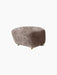 Three-quarter view of The Tired Man Ottoman in Sahara sheepskin, a fluffy footstool with short legs and front brass castors