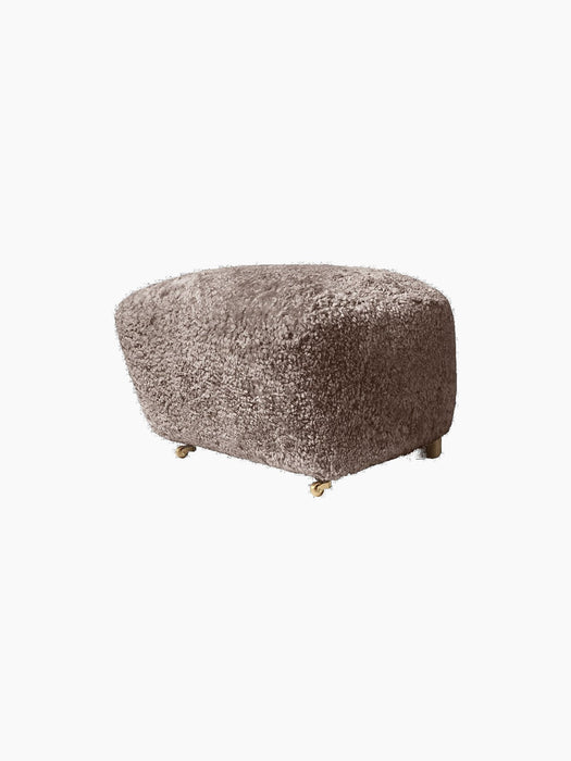 The Tired Man Ottoman upholstered in tactile Sahara sheepskin. The footstool has dark stained oak legs and brass castors.