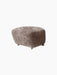 The Tired Man Ottoman upholstered in tactile Sahara sheepskin. The footstool has dark stained oak legs and brass castors.