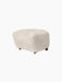 The Tired Man Ottoman, upholstered in plush Moonlight sheepskin with dark stained oak legs and small brass front wheels.