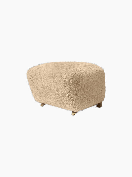 A side view of The Tired Man Ottoman upholstered in plush, honey-coloured sheepskin, set against a black background.