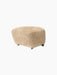 A side view of The Tired Man Ottoman upholstered in plush, honey-coloured sheepskin, set against a black background.