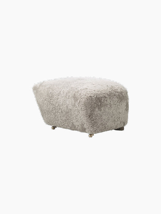 Three-quarter view of The Tired Man Ottoman in plush Green Tea Sheepskin, highlighting its soft texture on a black background