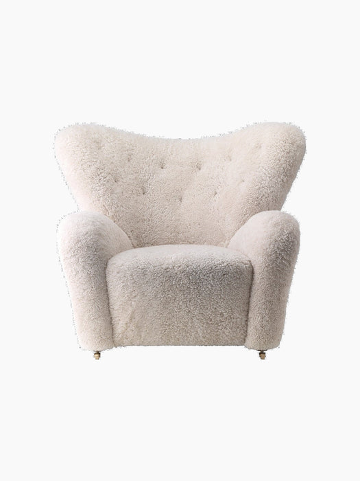Front view of The Tired Man Lounge Chair upholstered in plush, off-white sheepskin, with a high, curved, button-tufted back.