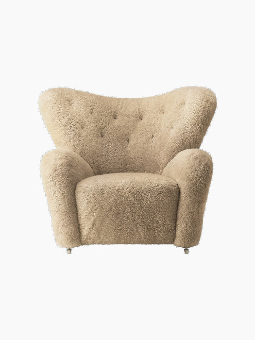 Front view of The Tired Man Lounge Chair in honey sheepskin. It features a curved, tufted back, plush arms and brass casters.