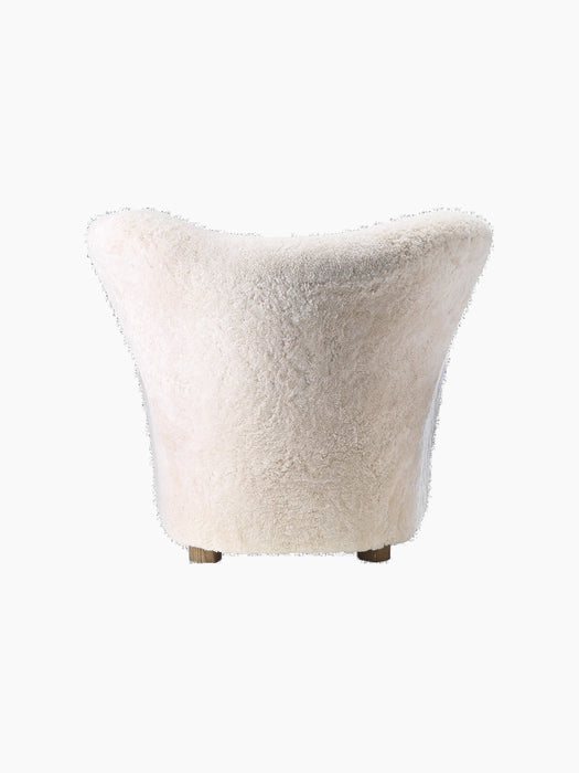 A back view of The Tired Man Lounge Chair, upholstered in plush, off-white sheepskin against a black background.