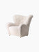 Side view of The Tired Man Lounge Chair in off-white sheepskin, showing its curved high back, large arms, and brass wheels.