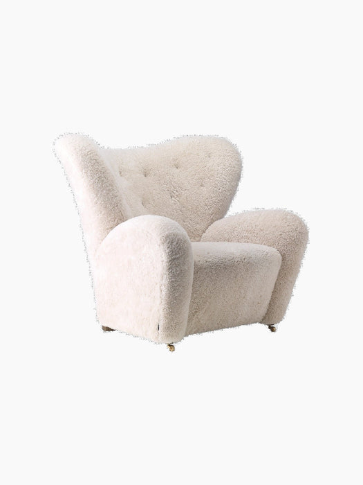 The Tired Man Lounge Chair, upholstered in off-white sheepskin, shown from a three-quarter angle against a black background.